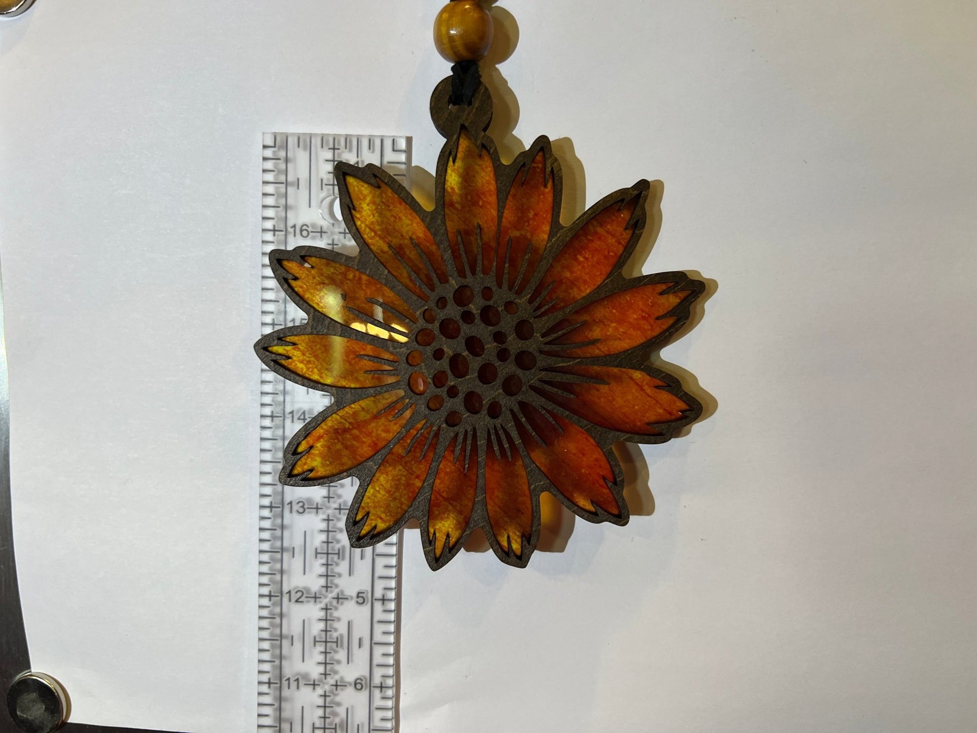 Sunflower suncatcher made of walnut stained wood and yellow acrylic, 4.5 inches in size, against white background.
