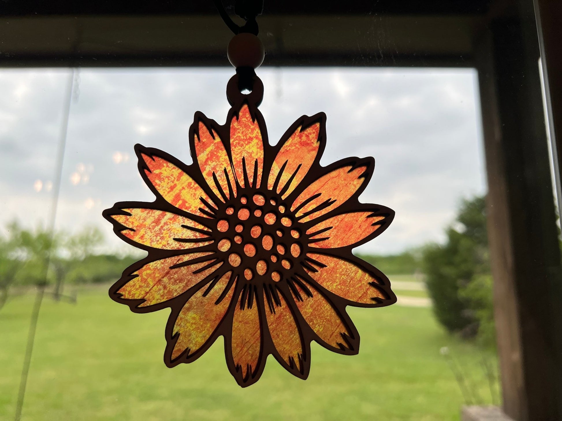 Sunflower suncatcher made of walnut stained wood and yellow acrylic, 4.5 inches in size, hanging in sunlight.