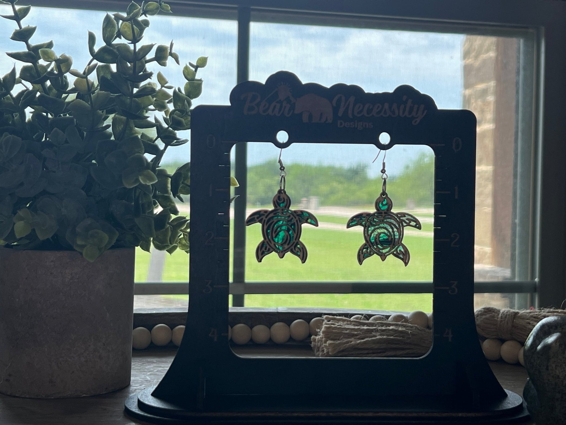 Pair of turtle-shaped stained glass effect wood and acrylic earrings in natural wood and multicolor in sunlight.