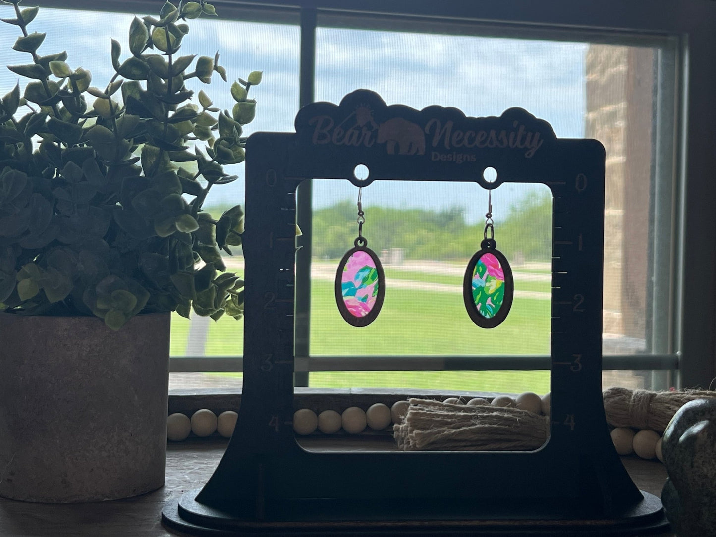 Pink floral suncatcher earrings with wood and acrylic materials, rustic style in sunlight.