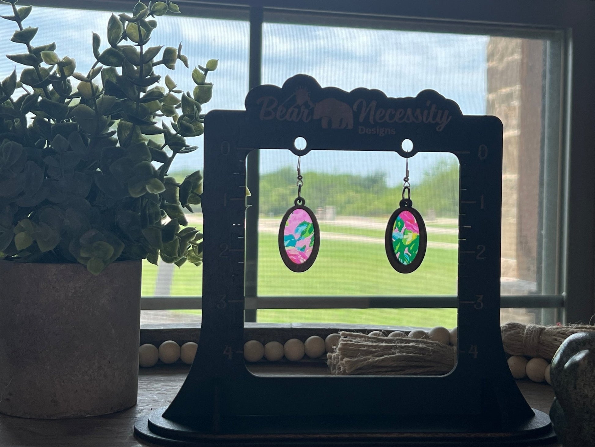 Pink floral suncatcher earrings with wood and acrylic materials, rustic style in sunlight.