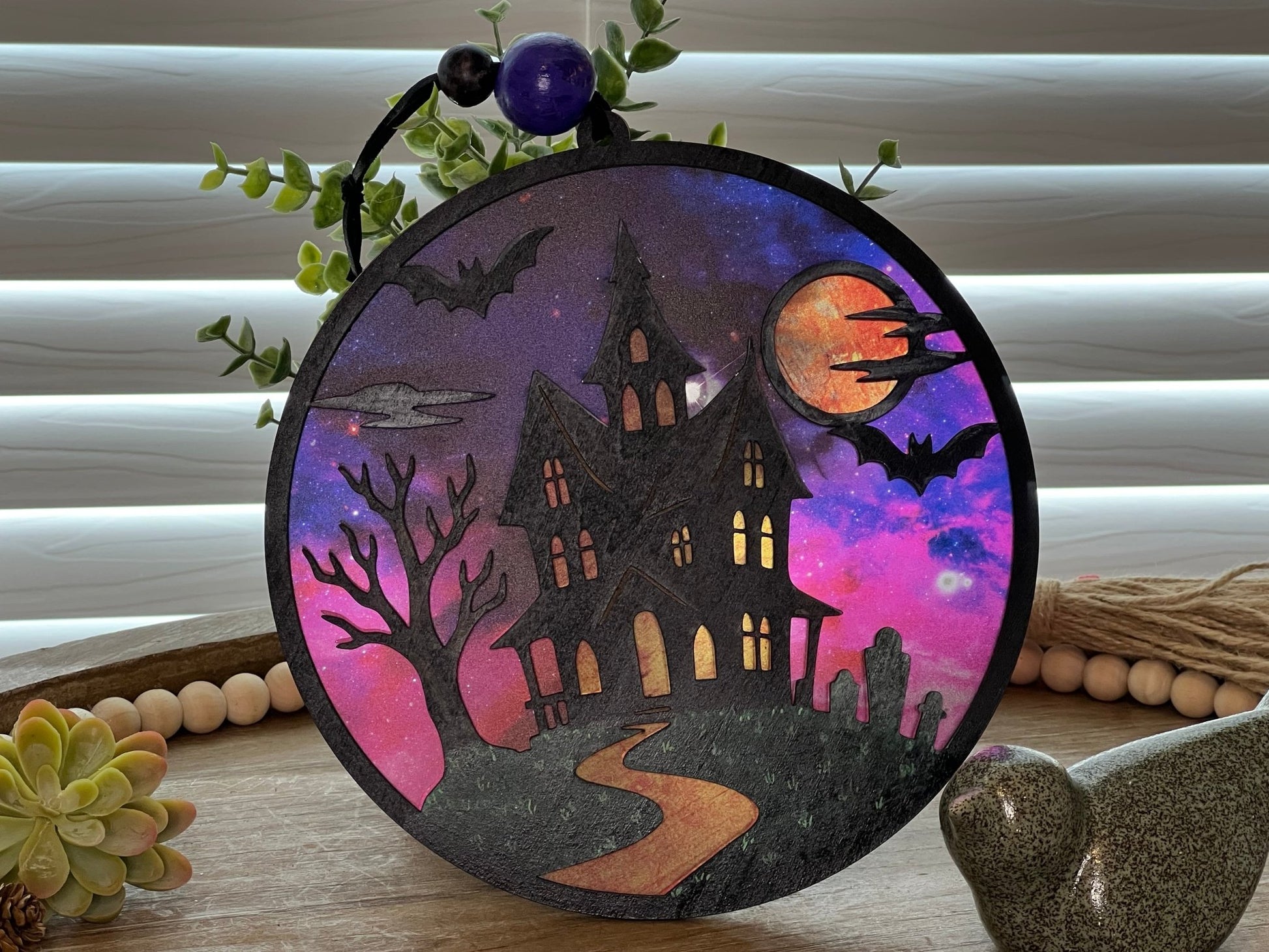 Hand painted suncatcher with a haunted house design on wood and acrylic, in vibrant colors - window closed.