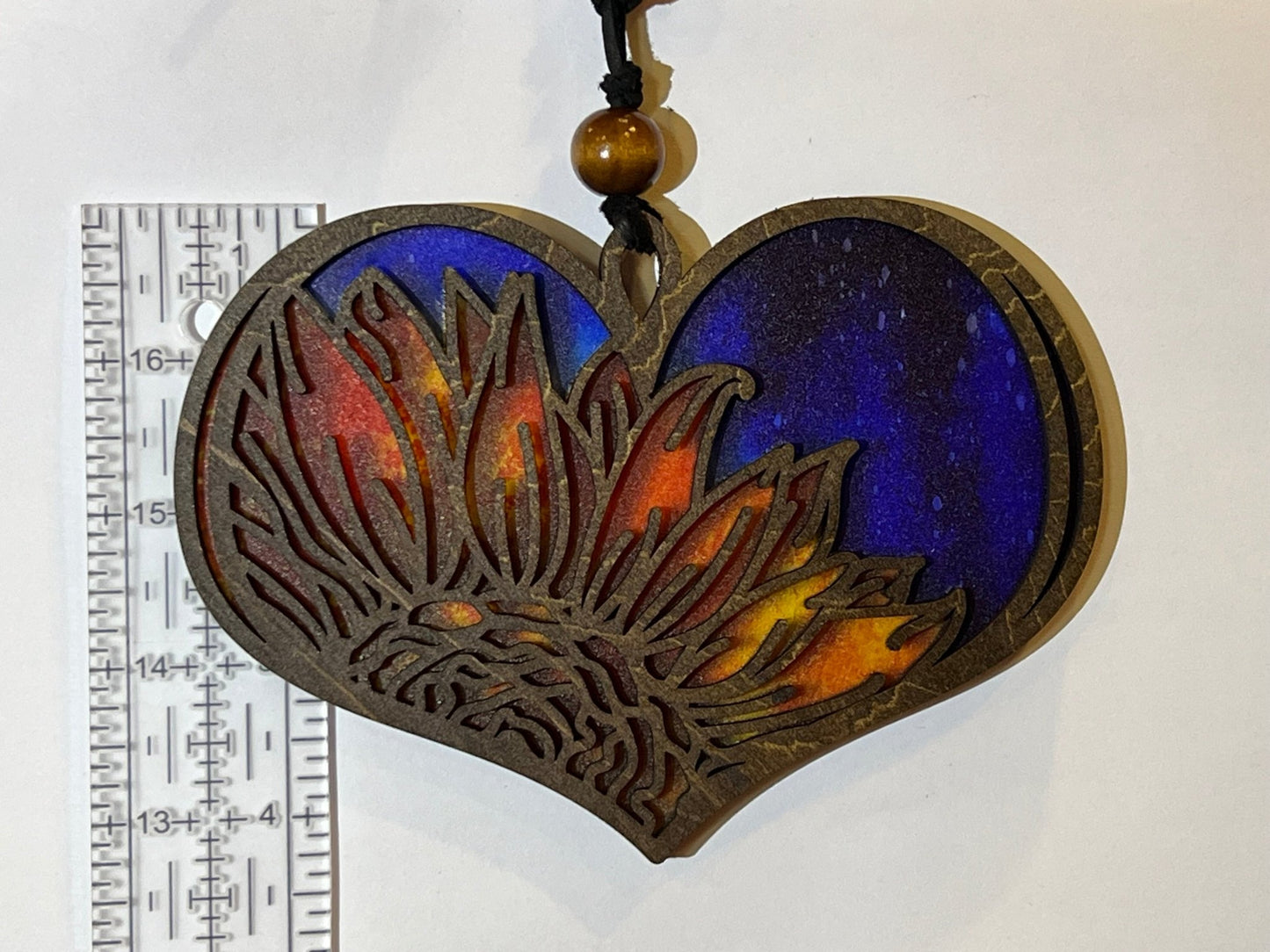 Heart-shaped suncatcher with sunflower design made of wood and multicolor acrylic, creating a stained glass effect.