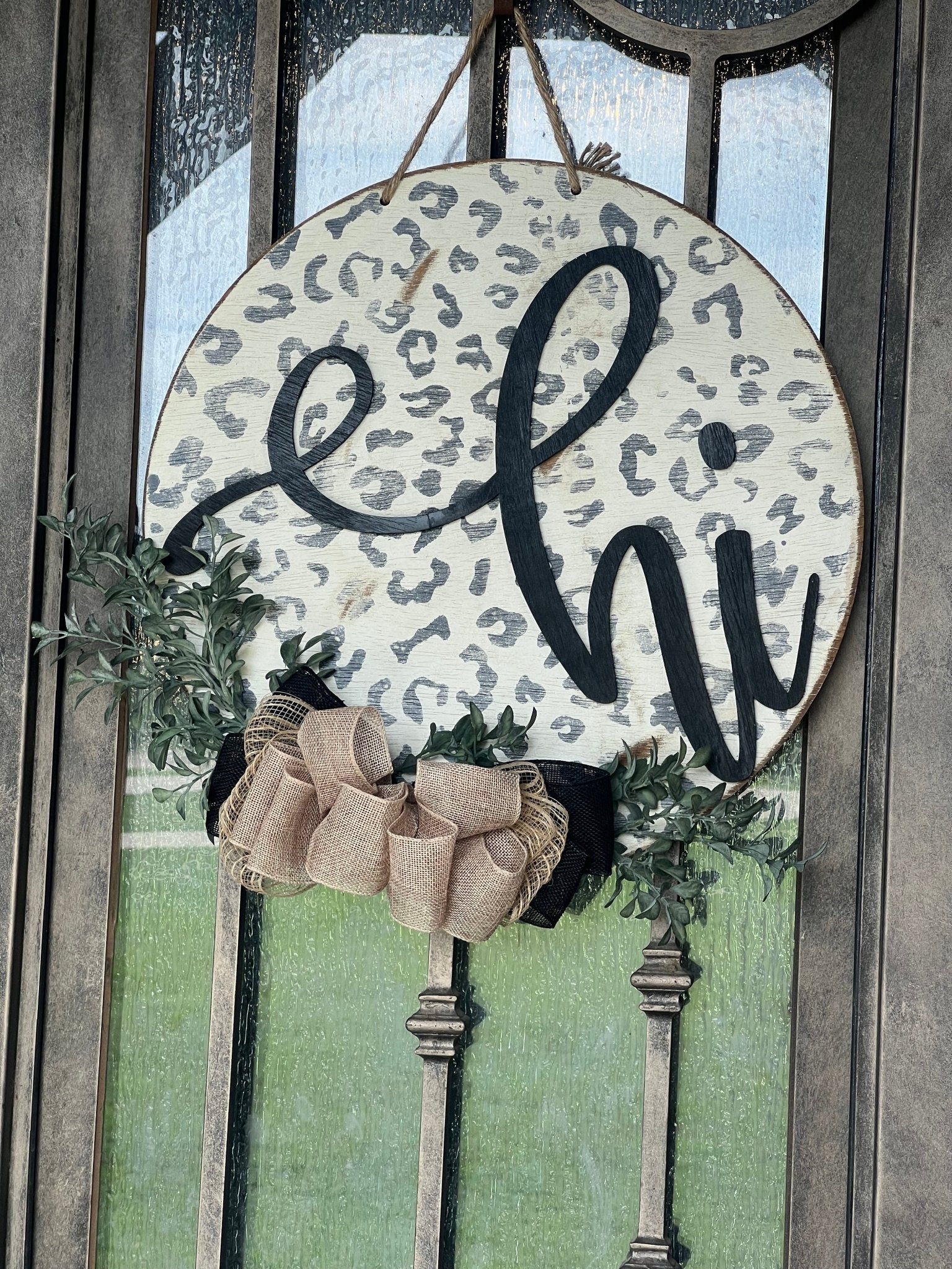 White leopard print door hanger made of wood, featuring a round shape and rustic-modern style. on metal door.