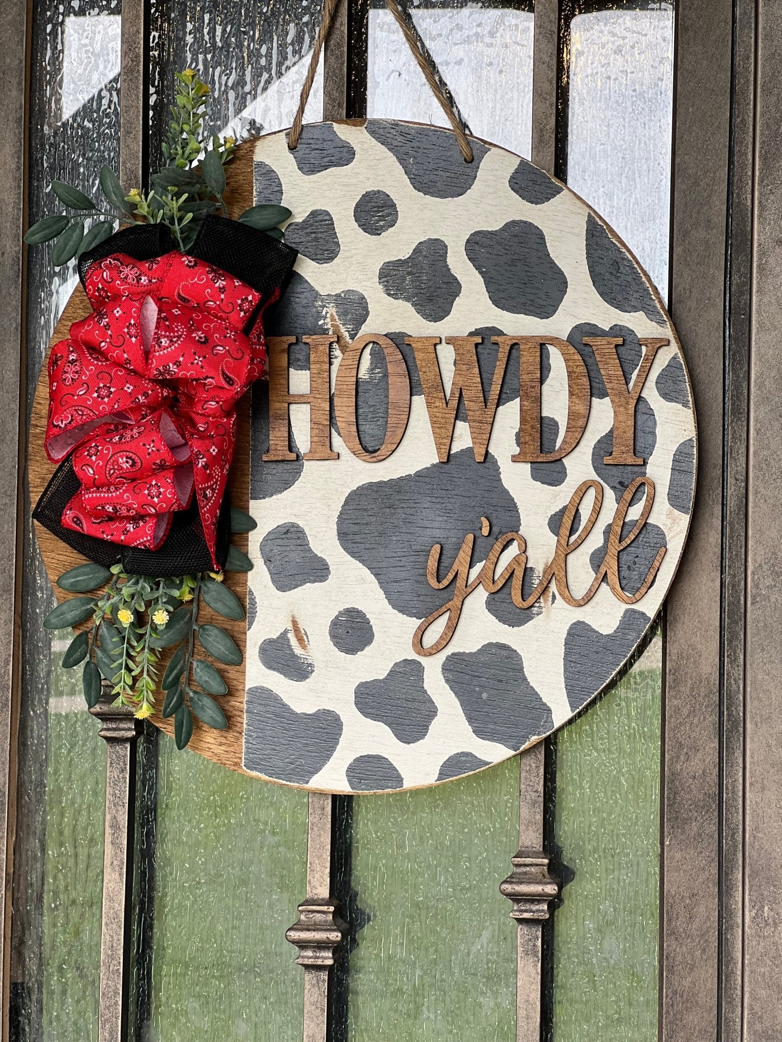 Cow Print Howdy Y’all Wood Door Hanger in black, red, and white with rustic charm hanging on a metal door.