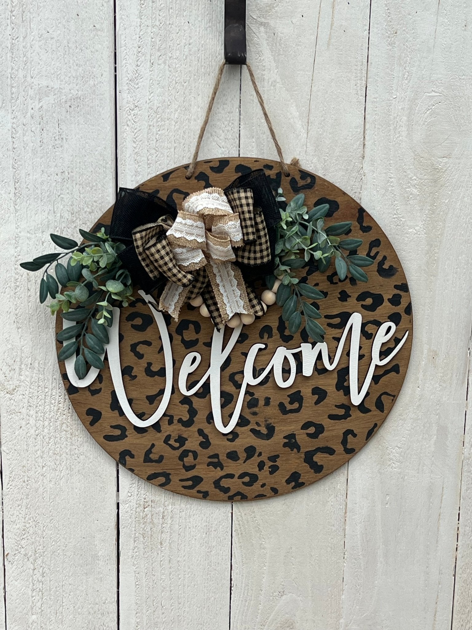 A rustic wooden door hanger with leopard print design, perfect for chic decor hanging on a white fence.