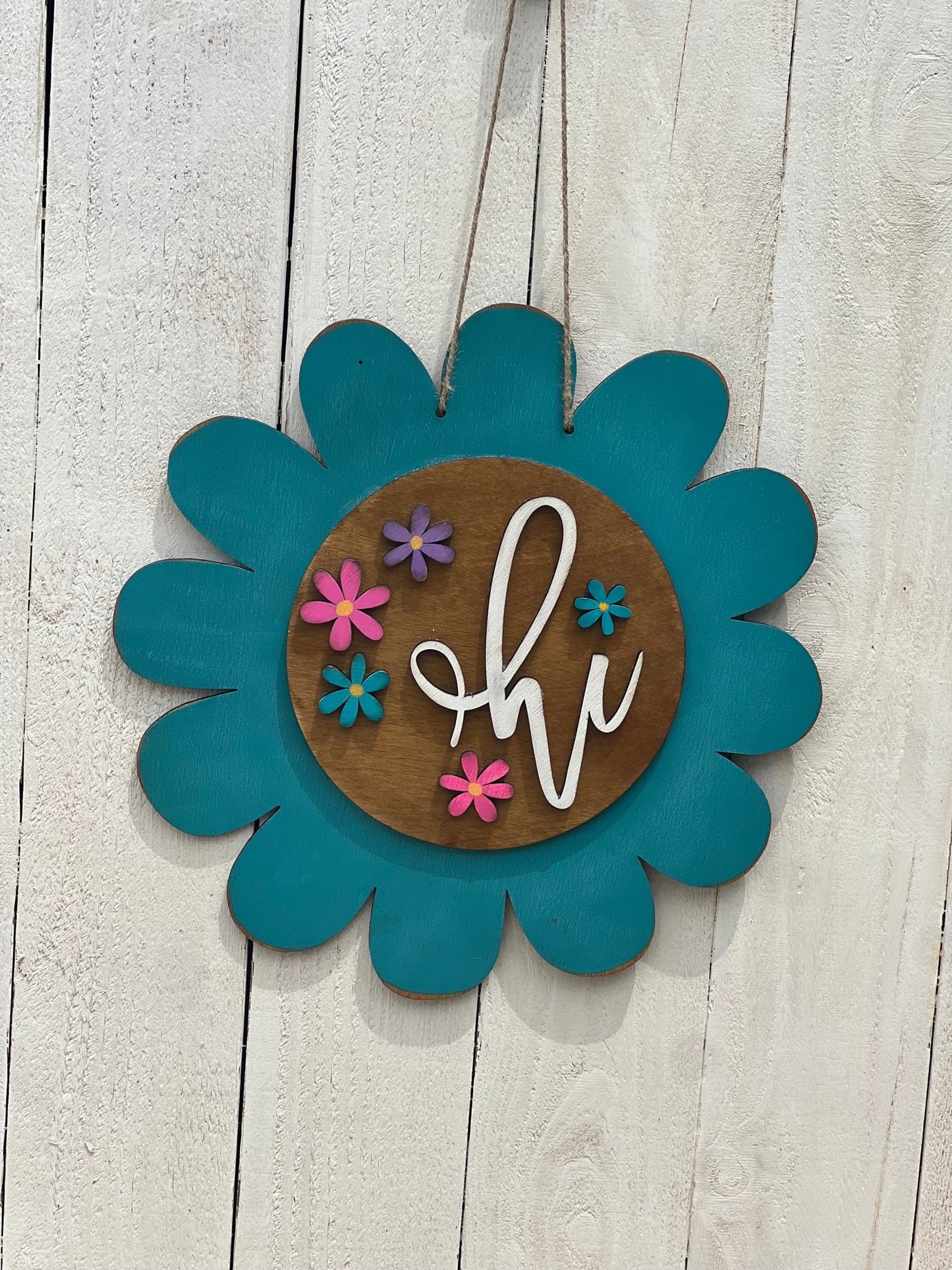 Turquoise flower door hanger made of natural wood with vibrant multicolor design on white fence.