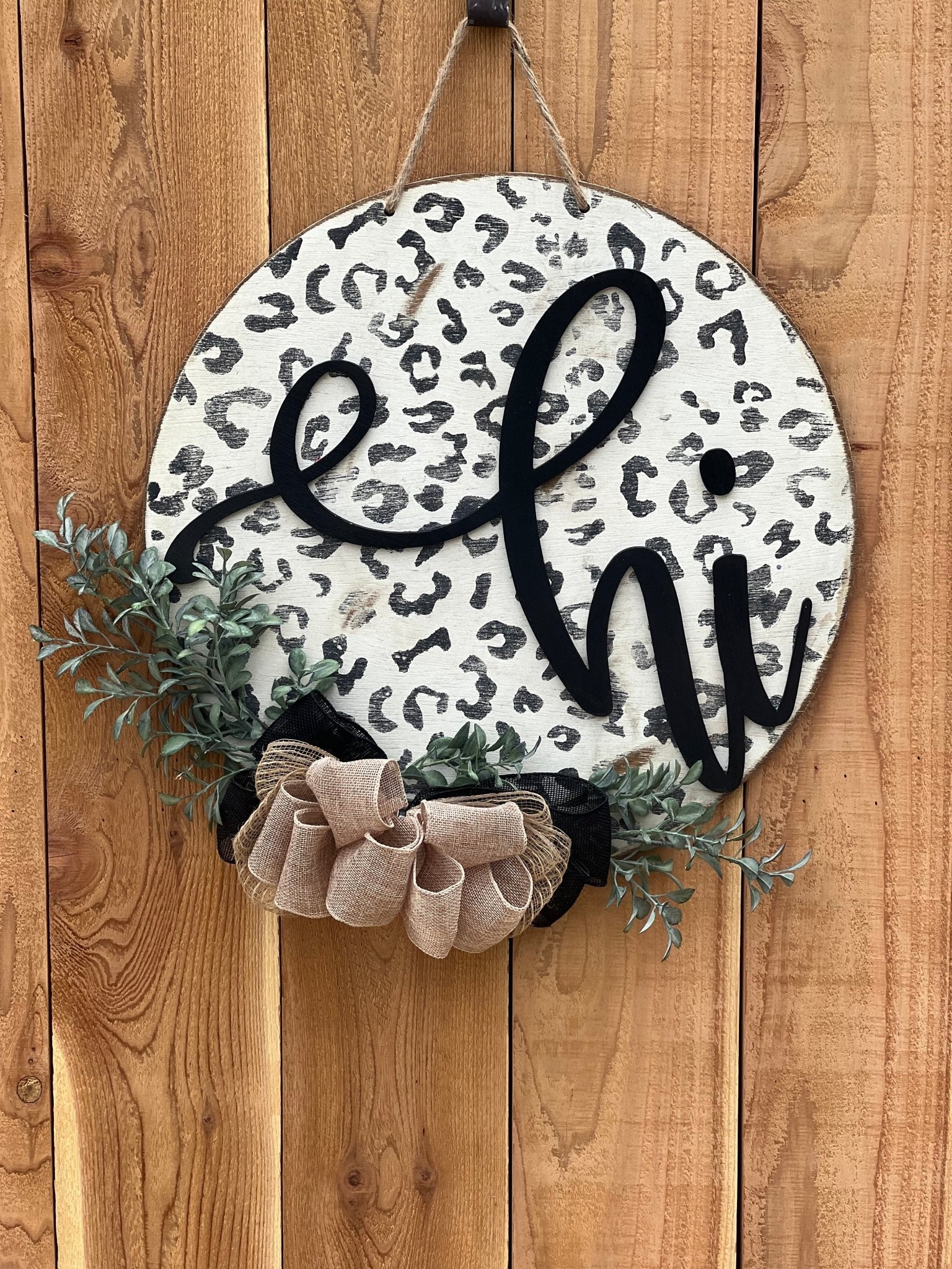 White leopard print door hanger made of wood, featuring a round shape and rustic-modern style on unpainted fence.