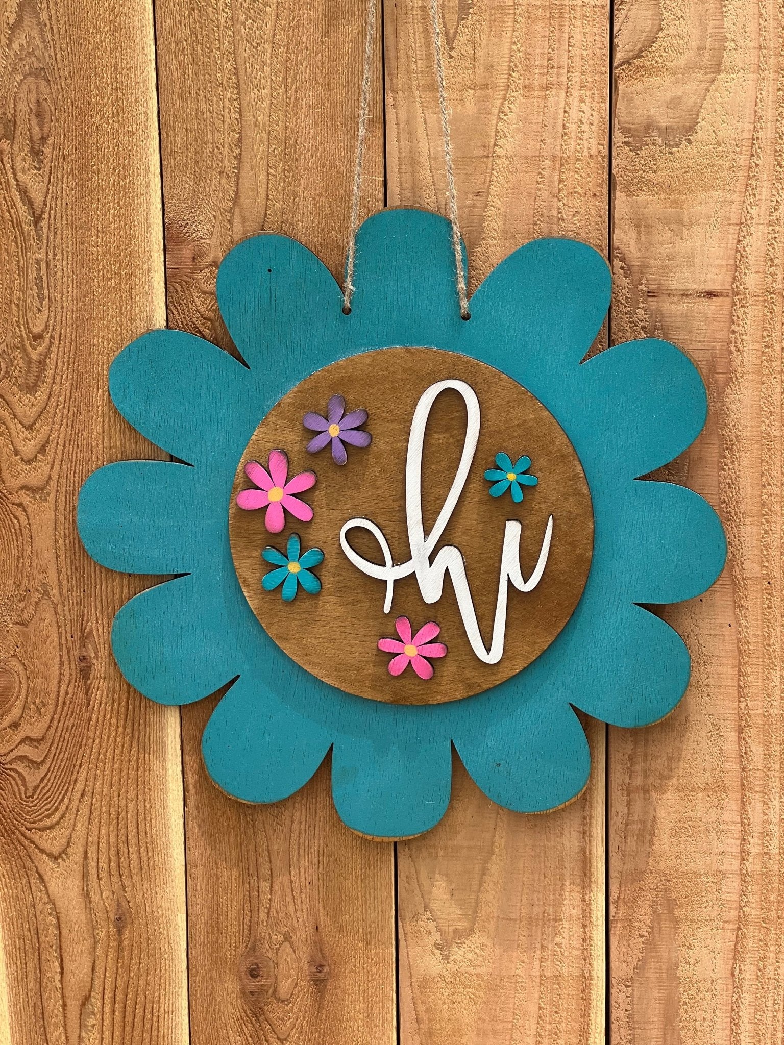 Turquoise flower door hanger made of natural wood with vibrant multicolor design on unpainted fence.