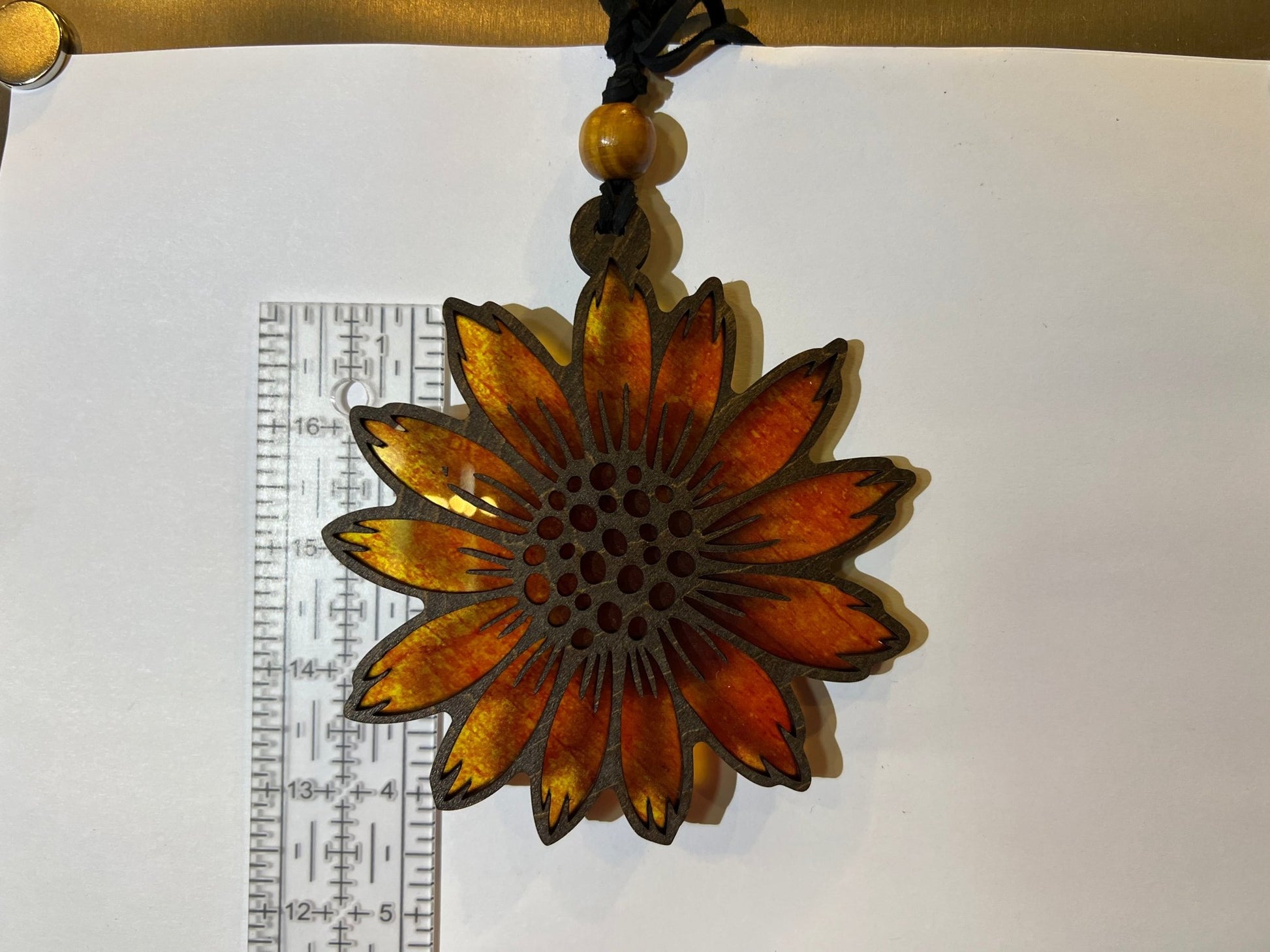 Sunflower suncatcher made of walnut stained wood and yellow acrylic, 4.5 inches in size, against white background with ruler.