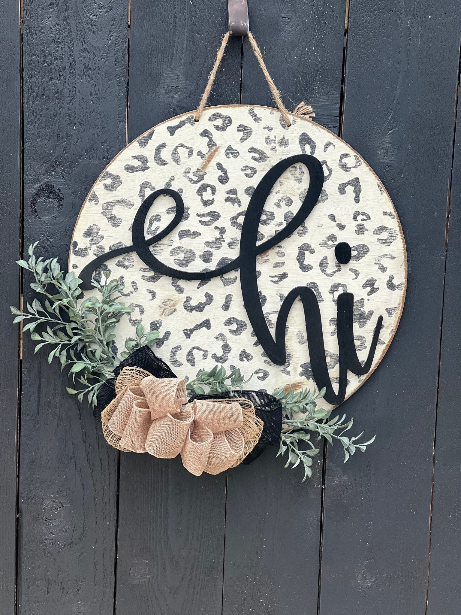 White leopard print door hanger made of wood, featuring a round shape and rustic-modern style on black fence.