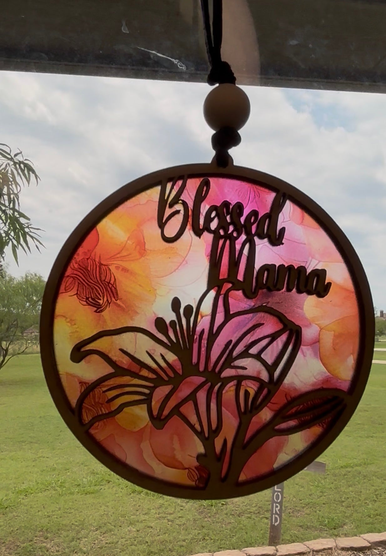 Handmade pink and coral Blessed Mama suncatcher with natural wood frame in sunlight.