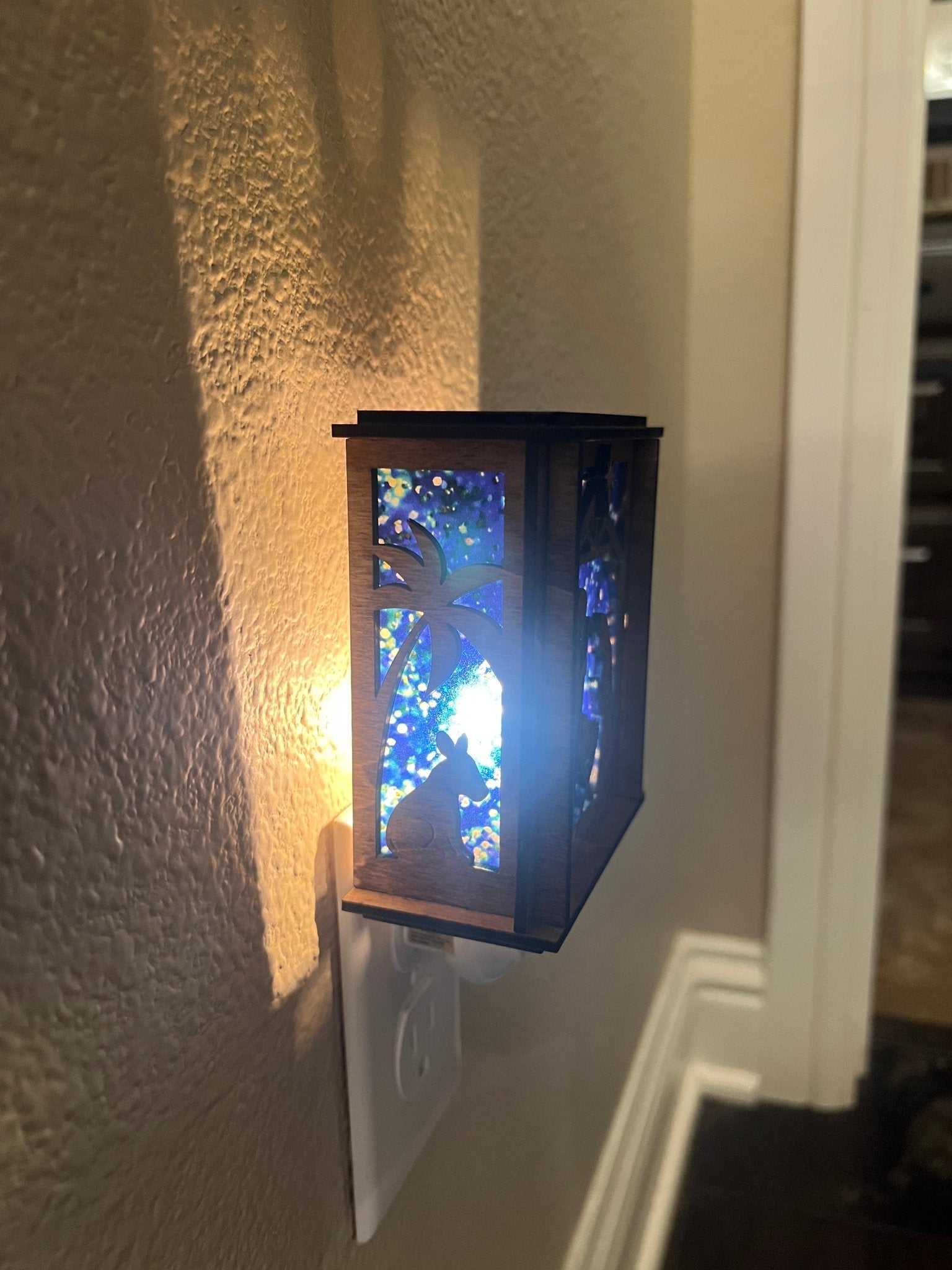 A Christmas Nativity Lantern Nightlight in golden oak with wood and acrylic materials - lit left side with lights on.