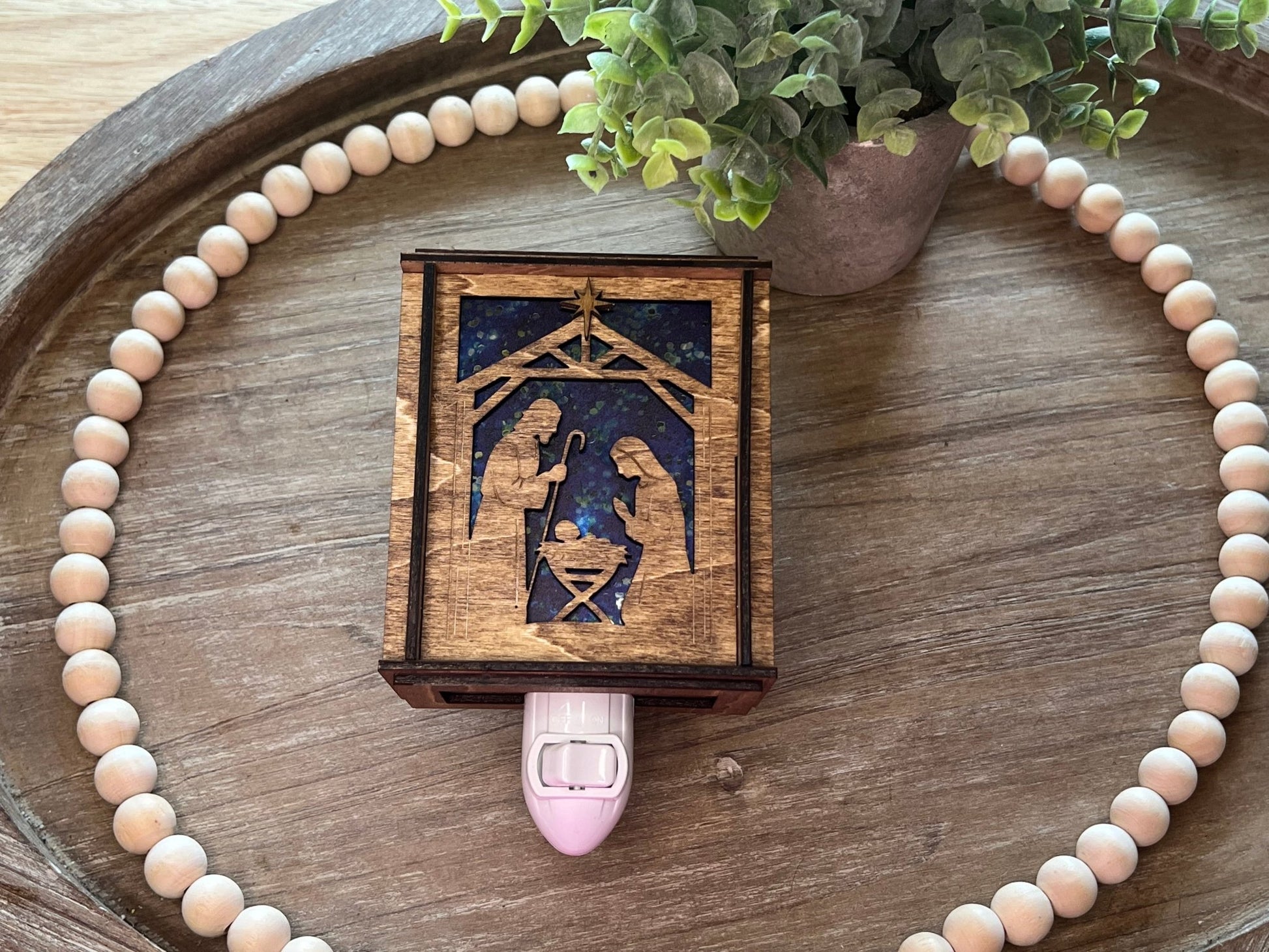 A Christmas Nativity Lantern Nightlight in golden oak with wood and acrylic materials - unlit laying on tray.