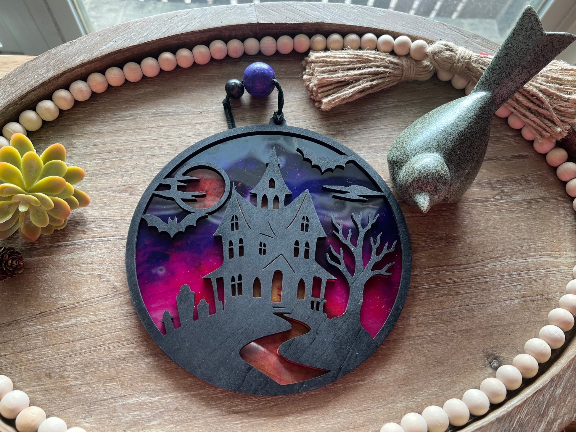 Hand painted suncatcher with a haunted house design on wood and acrylic, in vibrant colors back view on tray.