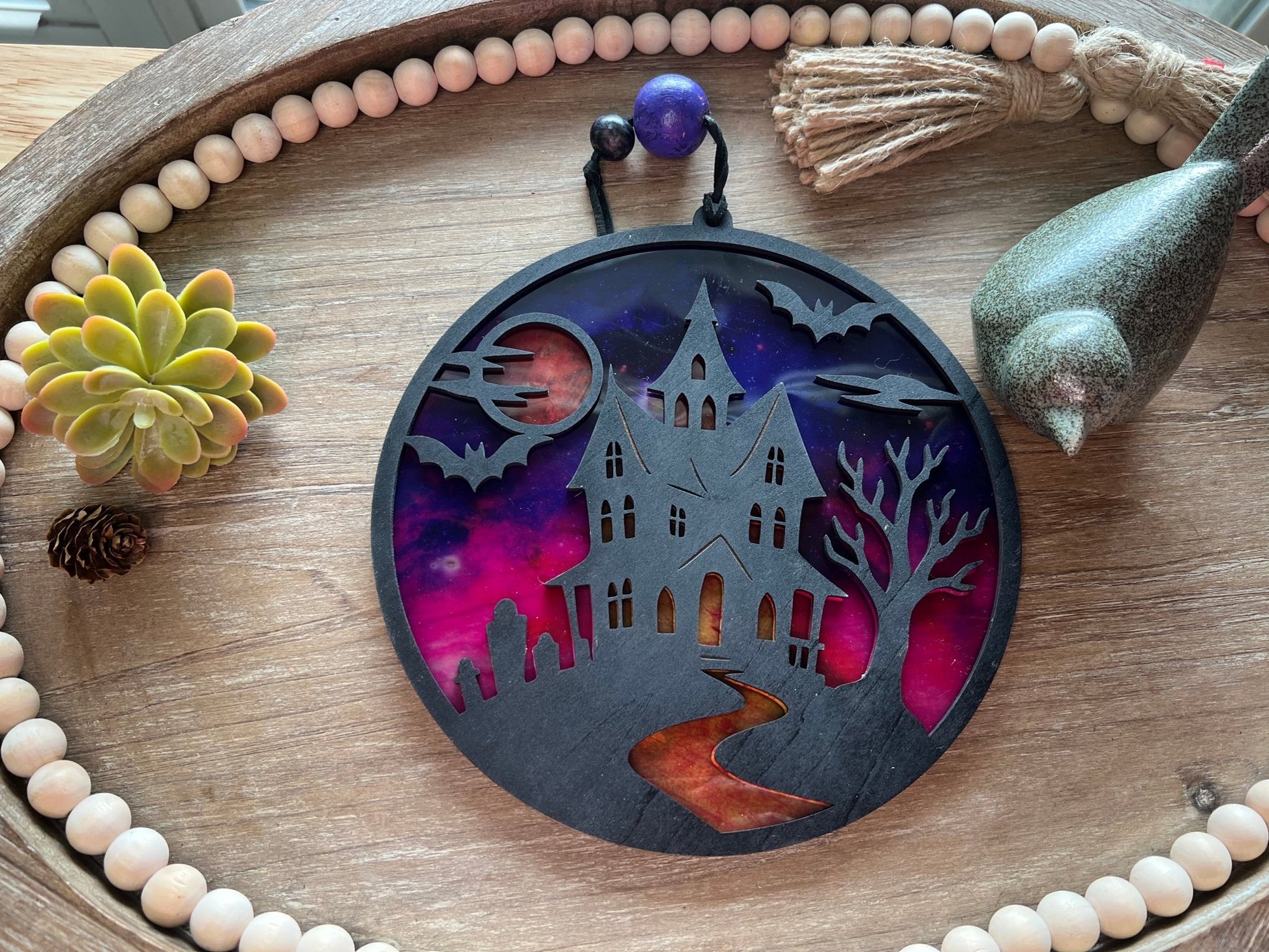 Hand painted suncatcher with a haunted house design on wood and acrylic, in vibrant colors laying on a tray back view.