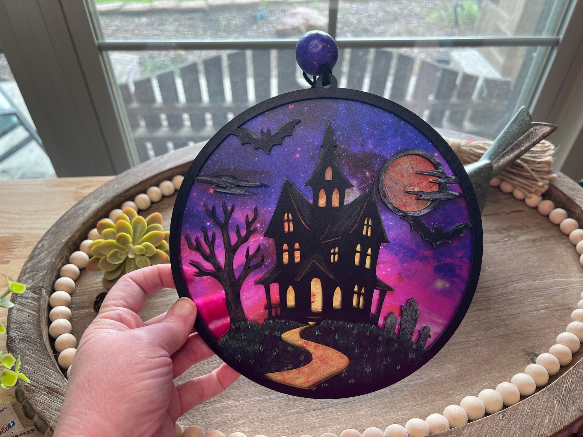 Hand painted suncatcher with a haunted house design on wood and acrylic, in vibrant colors in hand.