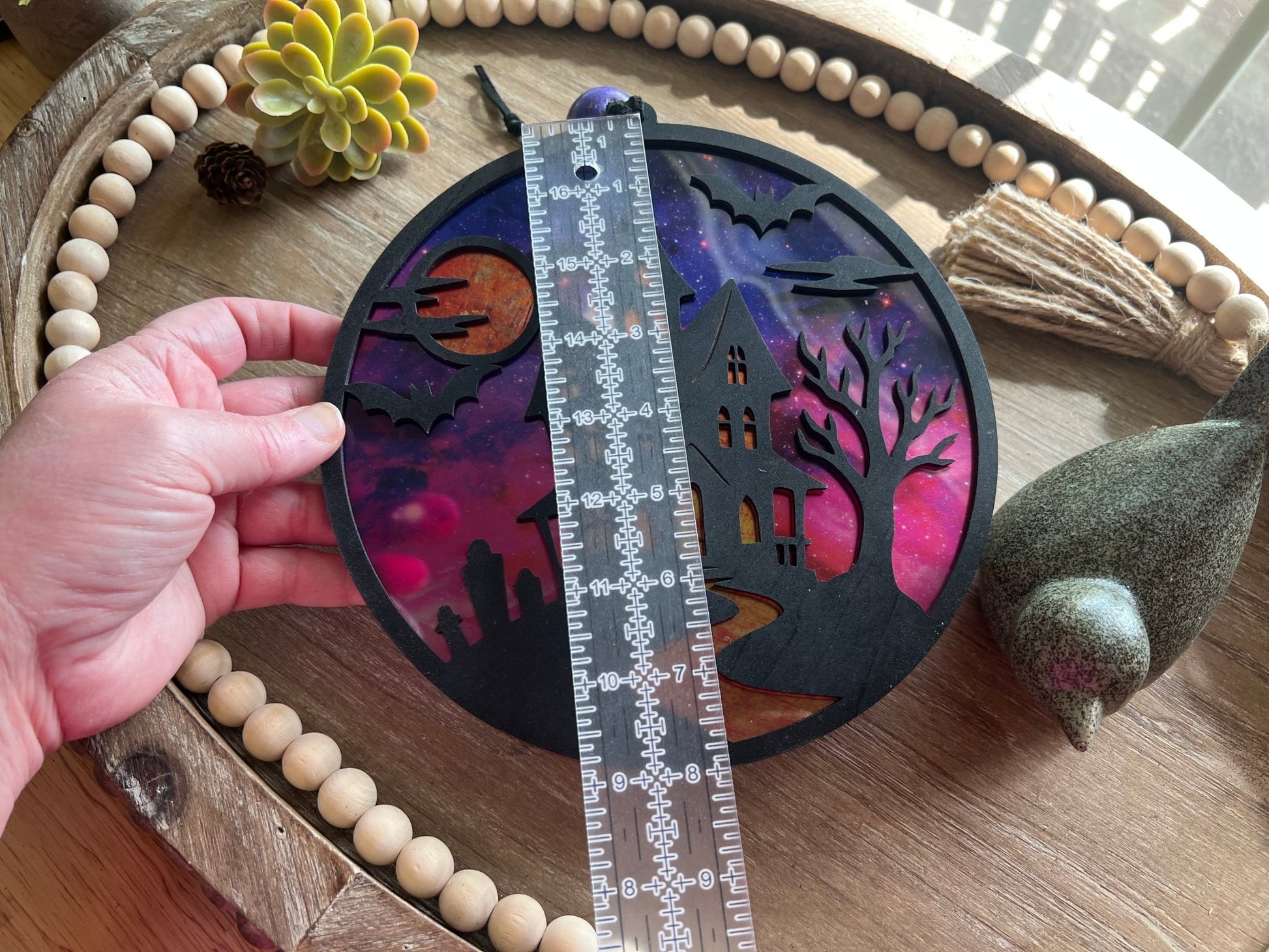 Hand painted suncatcher with a haunted house design on wood and acrylic, in vibrant colors with ruler for size reference.