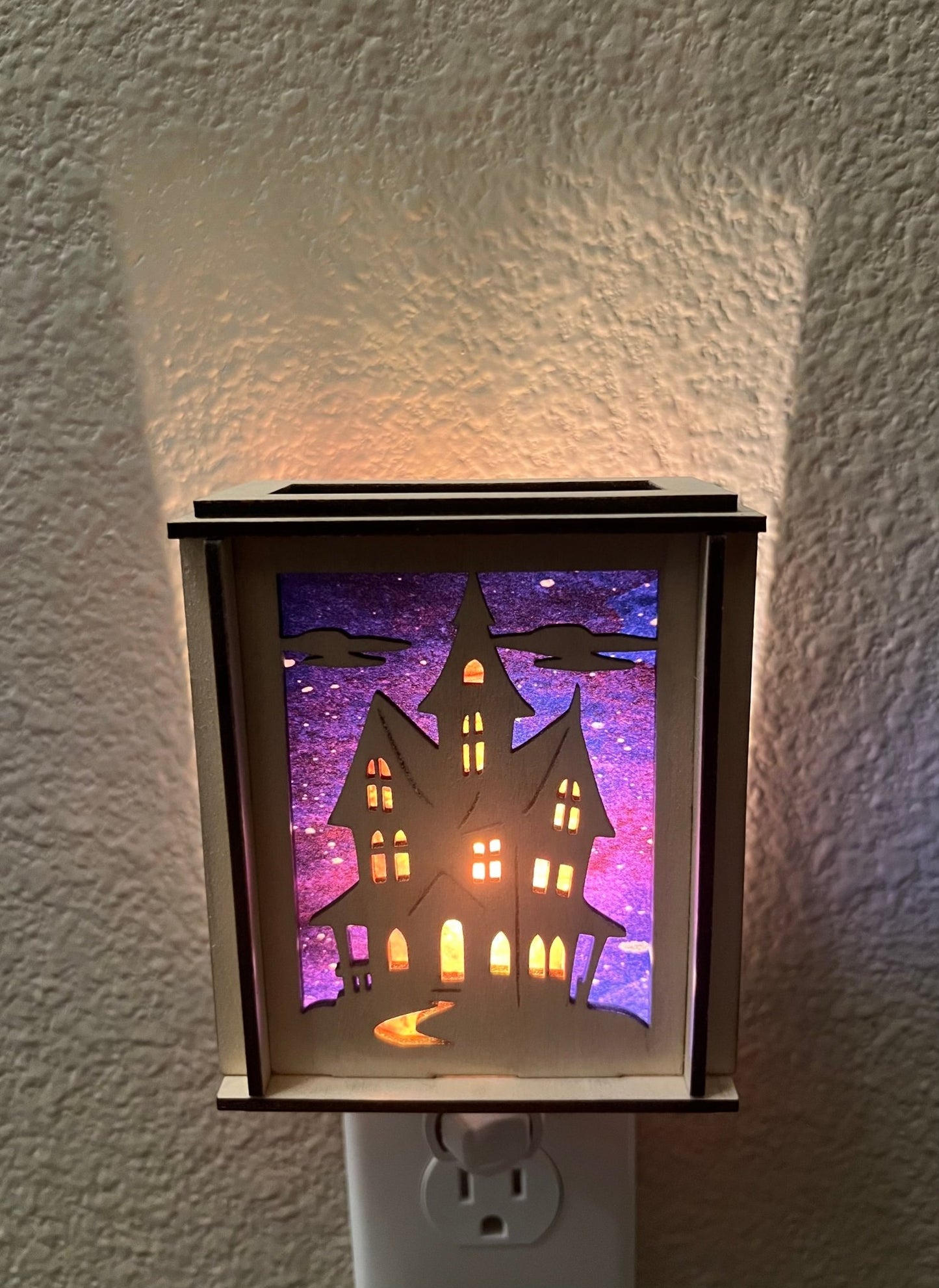 A haunted house-themed suncatcher with stained glass effect in black and multicolor acrylic - lighted from front.