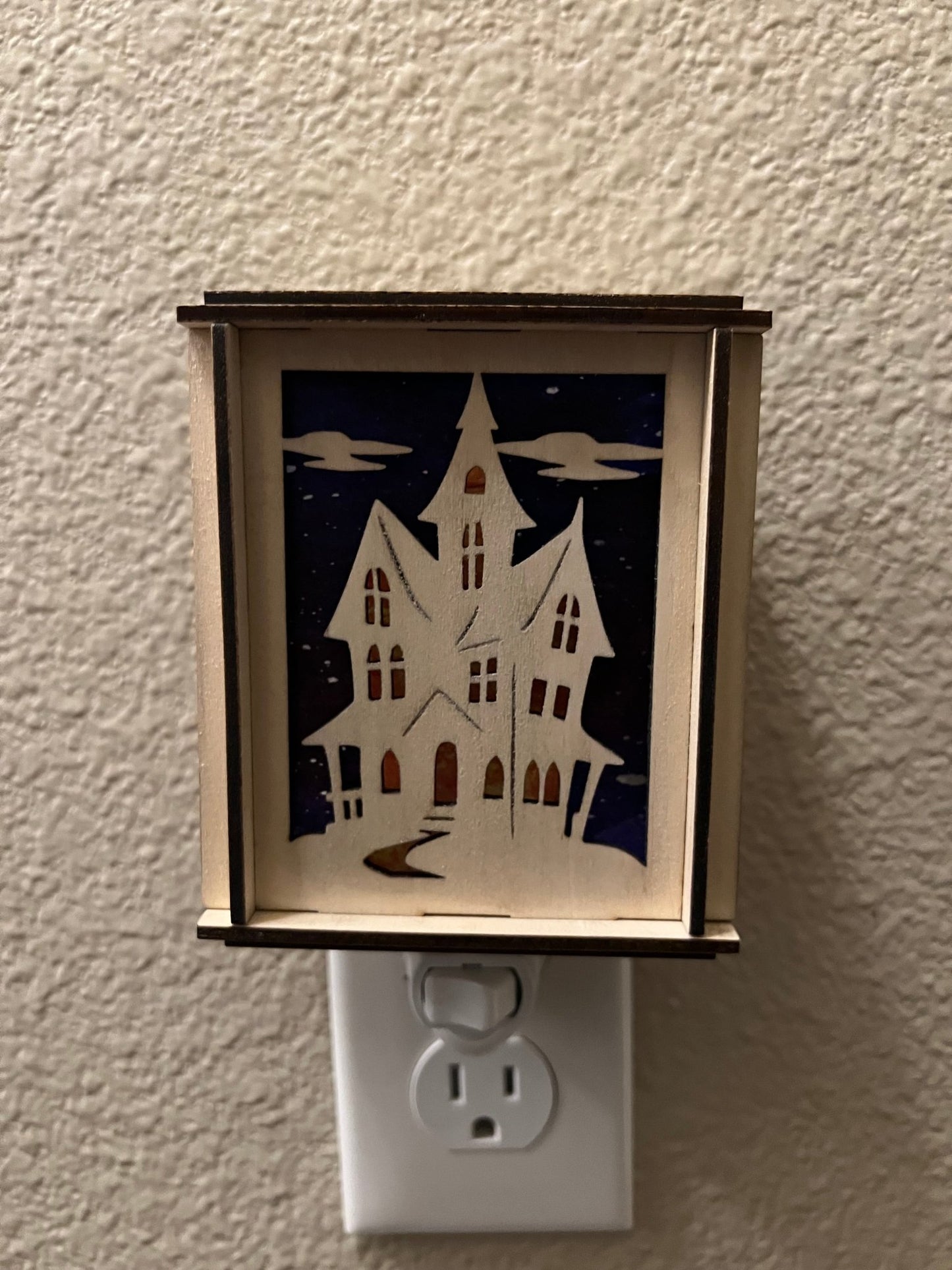 A haunted house-themed suncatcher with stained glass effect in black and multicolor acrylic from front.