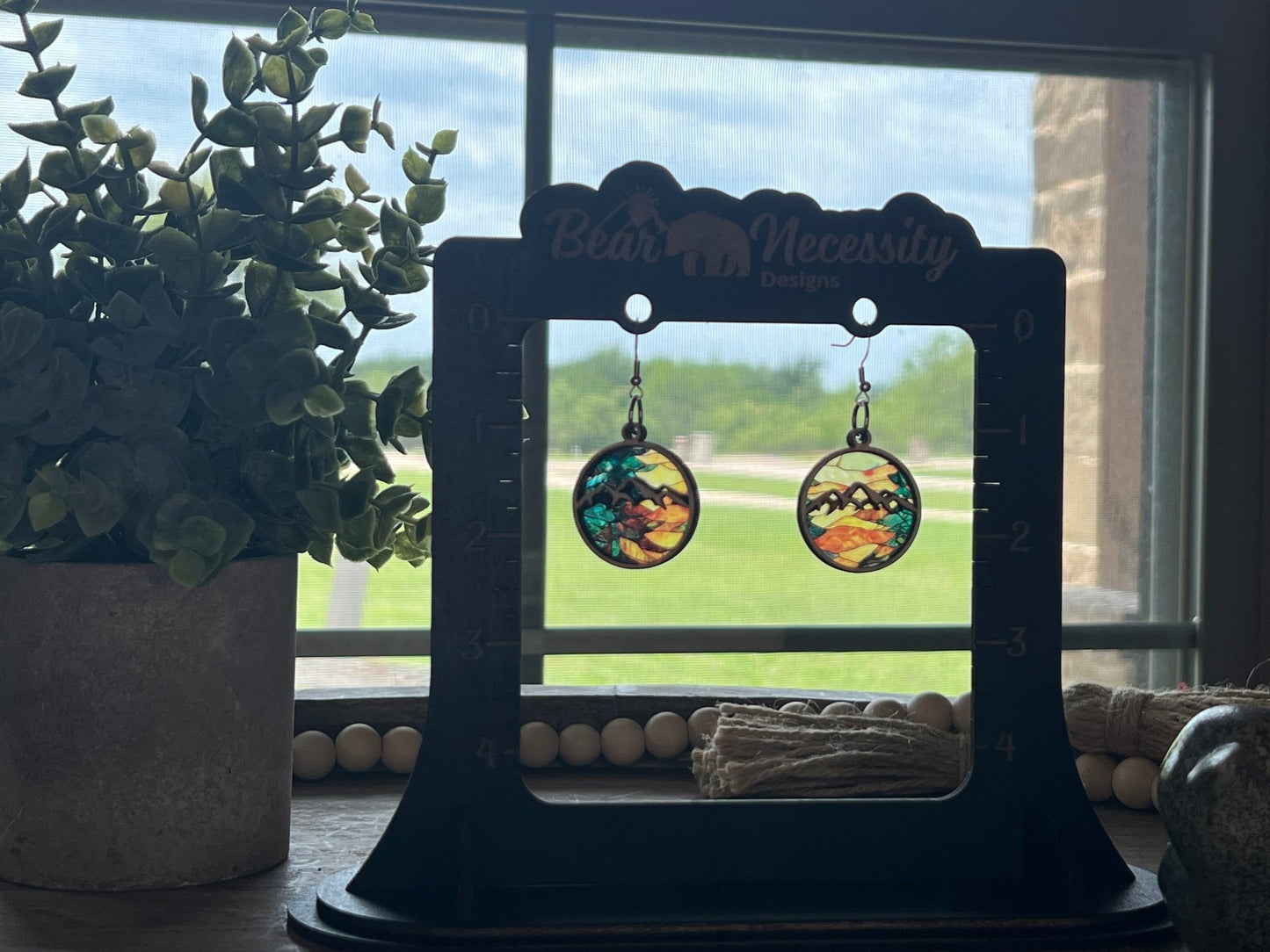 Handmade mountain suncatcher earrings with stained glass effect, featuring natural wood and multicolor acrylic in sun.