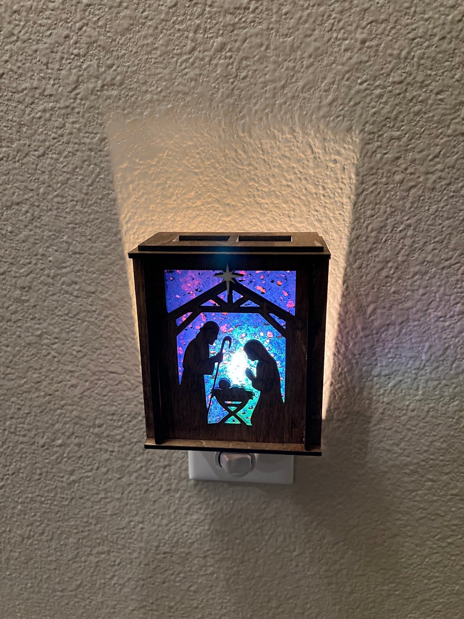 Golden oak stained wooden and acrylic nativity nightlight with rustic charm front view plugged in and lit.