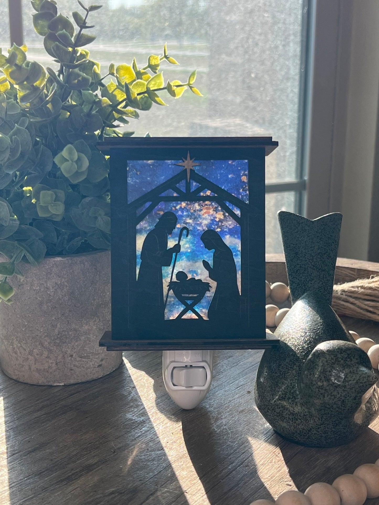 Rustic nativity nightlight lantern made of black wood and golden oak stained acrylic standingup  with front view and sunlit.