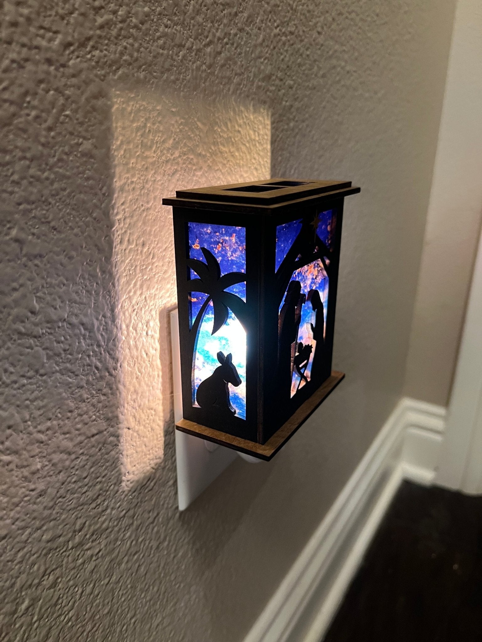 Rustic nativity nightlight lantern made of black wood and golden oak stained acrylic plugged in withleft view and lit.