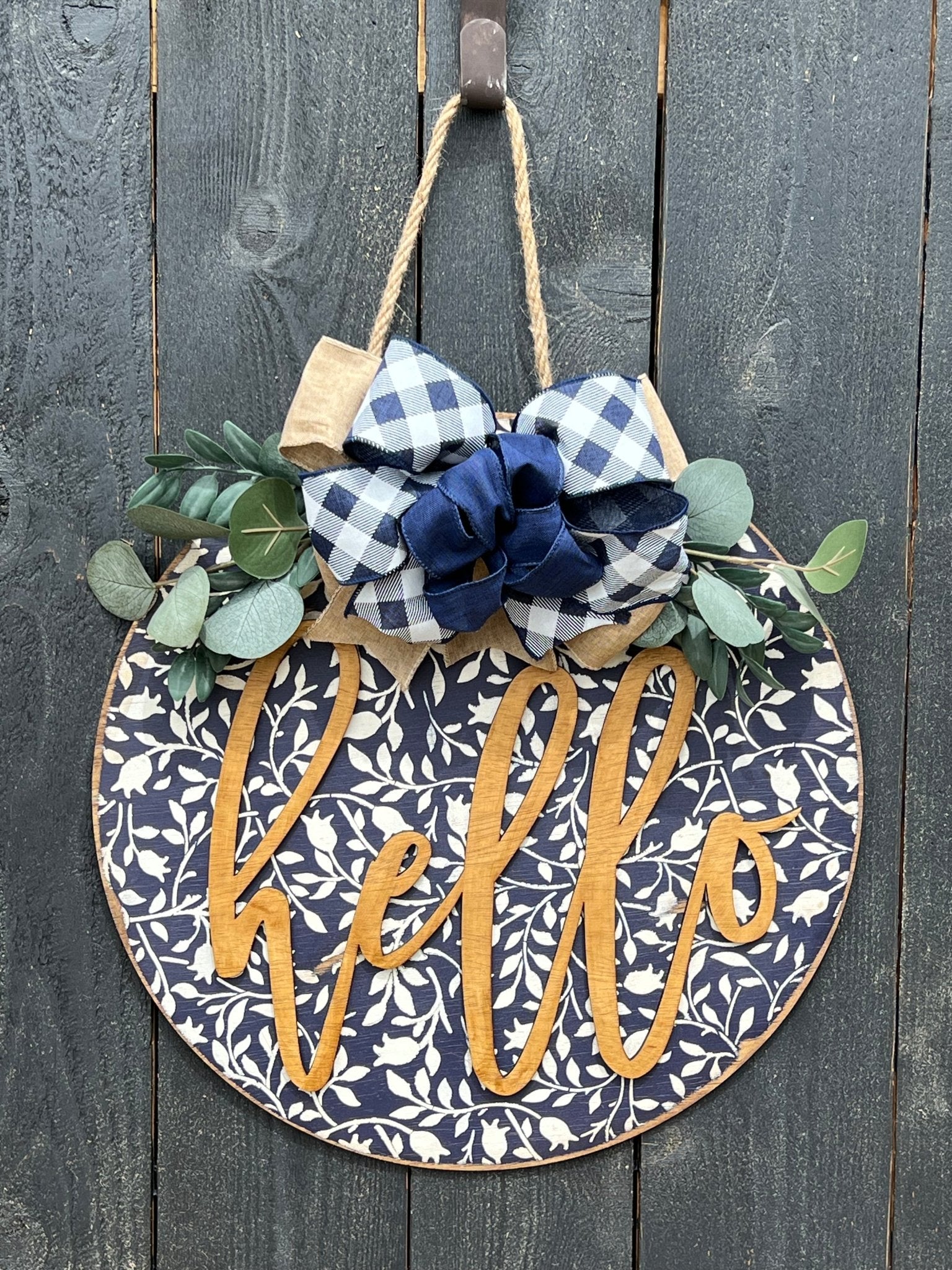 Navy wood hello door hanger with mini flowers on black fence, perfect for rustic entryway decor.