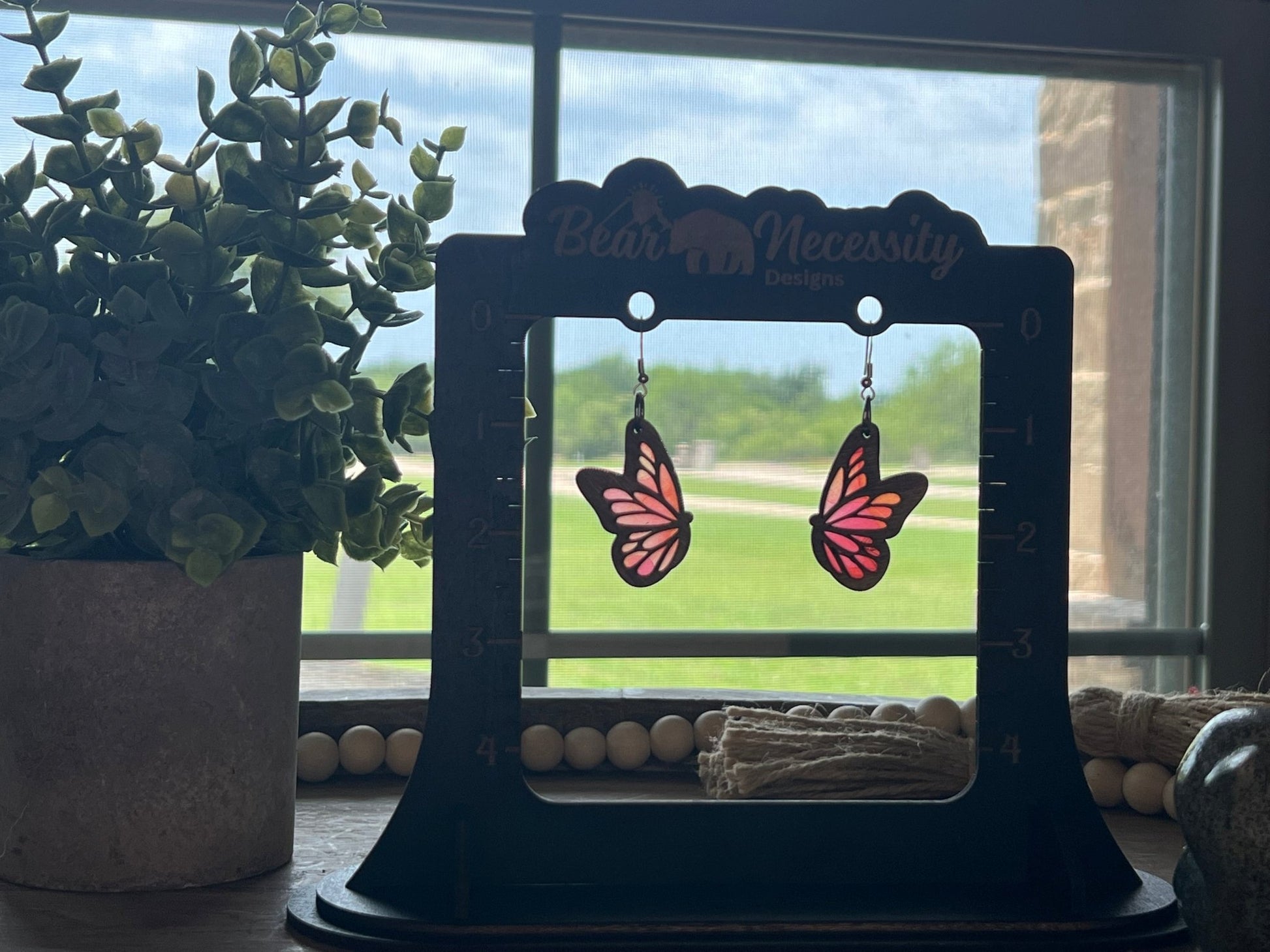 Pink and coral butterfly earrings with stained glass effect, crafted from wood and acrylic in sunlight.
