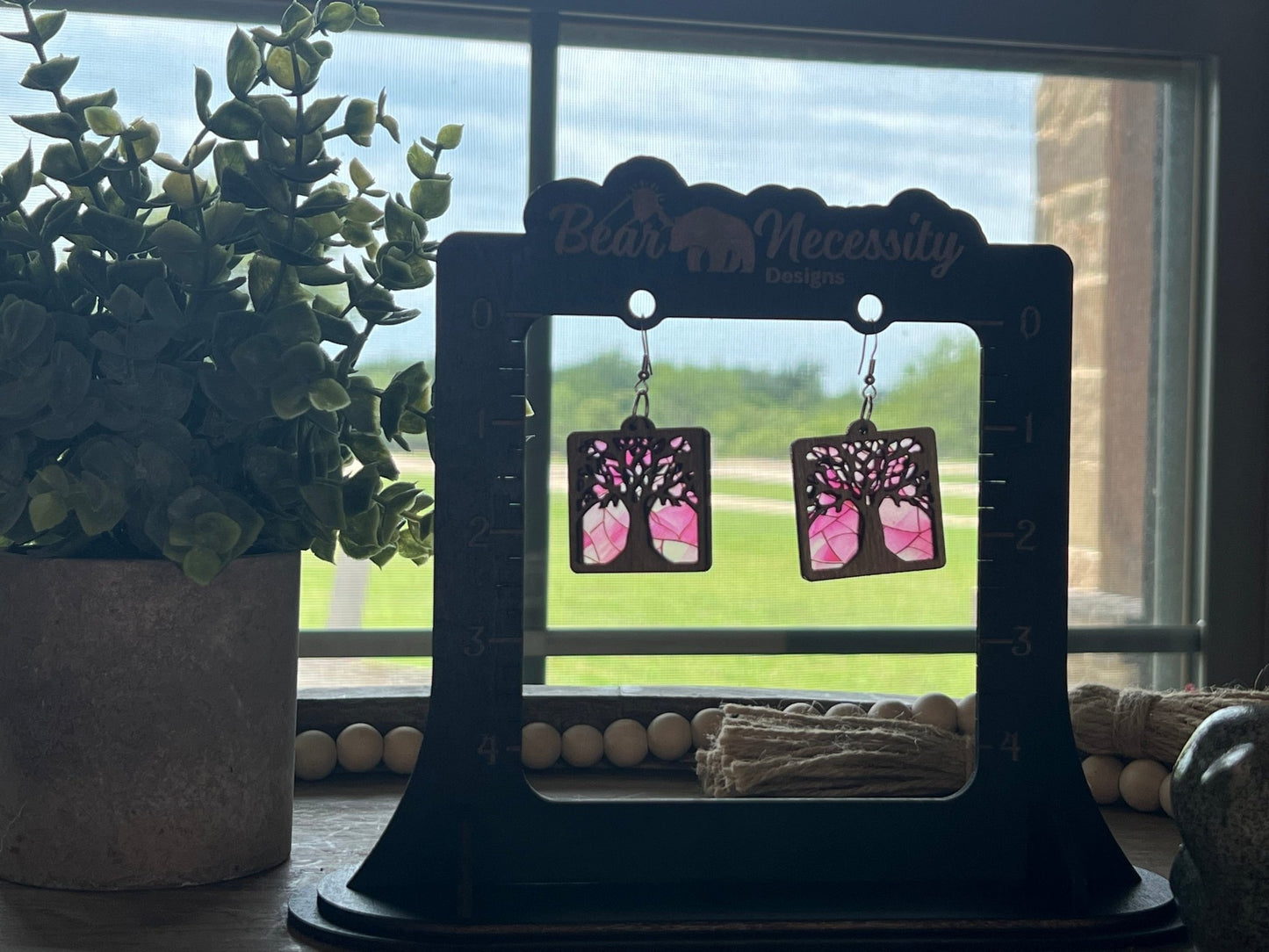 Tree of Life earrings with stained glass effect, made of wood and pink acrylic, in a rustic-modern style in sunlight.